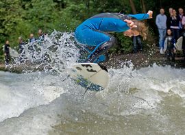 Surfer auf der Eisbachwelle Ein Surfer in blauem Neoprenanzug an der Eisbachwelle vor Zuschauern.